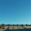 a professional roofing contractor stands on a steeply pitched roof with advanced tools and various roofing materials neatly arranged on the surface, showcasing the complexity and craftsmanship involved in estimating local roof replacement costs against a clear blue sky.