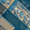 a dramatic overhead view of a commercial building with visible roof damage, including sagging sections and water accumulation, illuminated by stark artificial lighting to highlight the urgency of needed repairs.